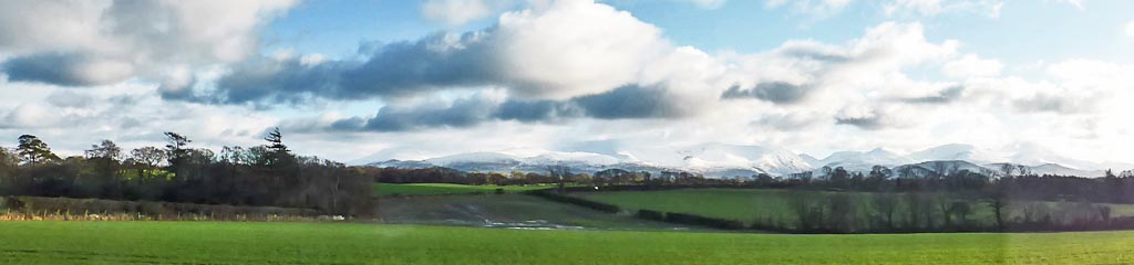 Snow on the mountains viewed from Llansadwrn across wet fields.